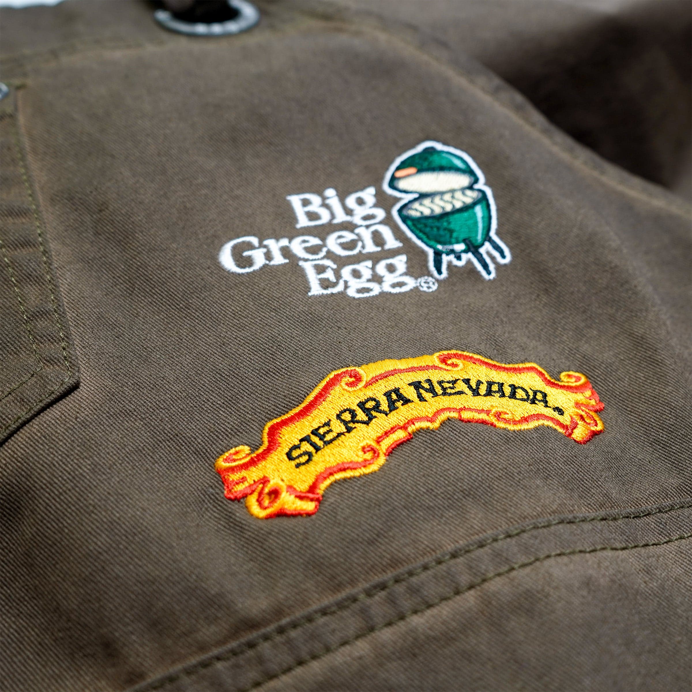 Close up angled view of the two embroidered brand logos on the Sierra Nevada Big Green Egg Grilling Apron